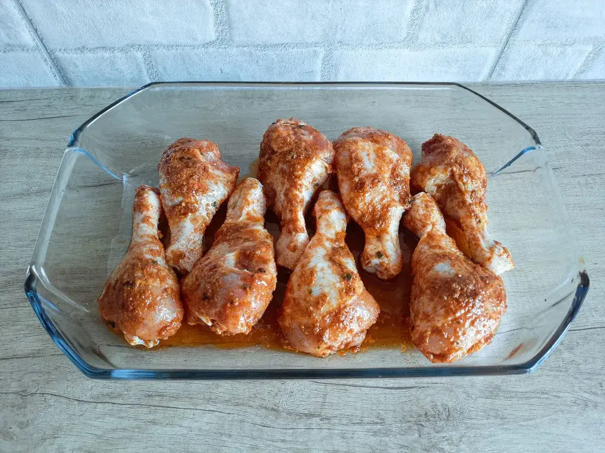 Gotowe do pieczenia pałeczki z kurczaka w szklanym naczyniu, doprawione aromatycznymi przyprawami.
