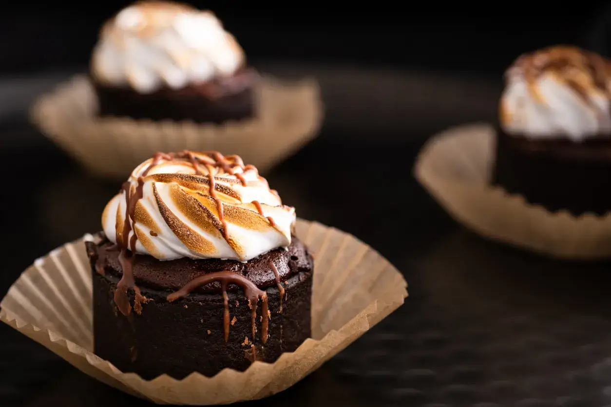 Pyszne babeczki brownie z pianką marshmallow i polewą czekoladową, kusząco wyglądające na ciemnym tle.