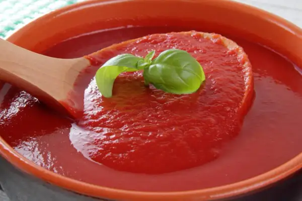 Gęsty, domowy ketchup z pomidorów malinowych, z listkiem bazylii na drewnianej łyżce.