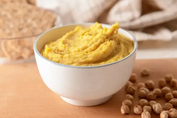 Puszysta pasta z ciecierzycy w miseczce, obok kilka ziaren ciecierzycy i chrupki.