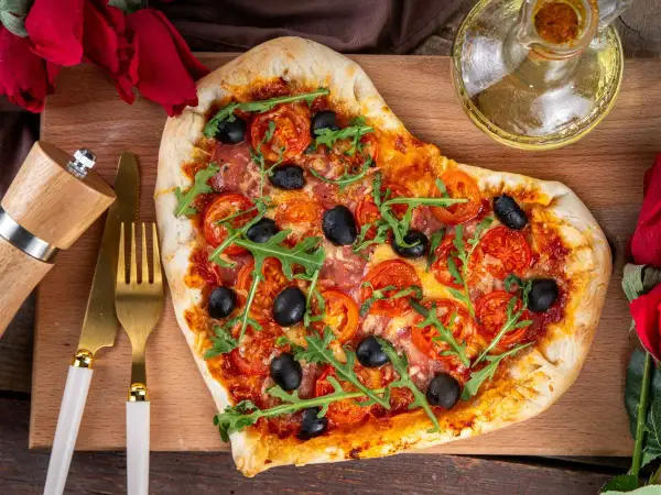 Serce z pizzy z rukolą i oliwkami, idealne na romantyczną kolację w domu. Obok złote sztućce i młynek do pieprzu.
