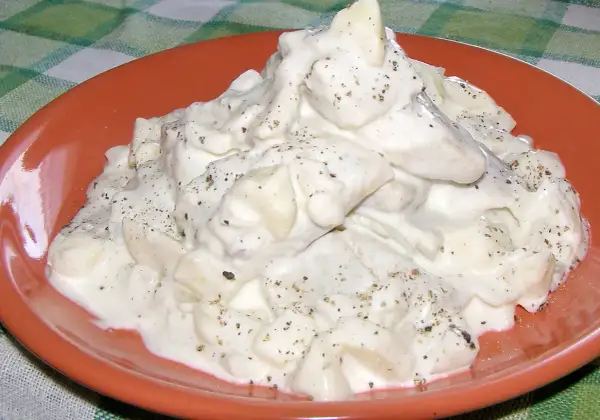 Pyszne śledzie w śmietanie, doprawione pieprzem, na pomarańczowym talerzu.