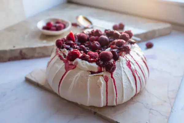 Jak piec beze? Puszysta Pavlova z kremem i wiśniami, ozdobiona syropem. Idealna na deser.