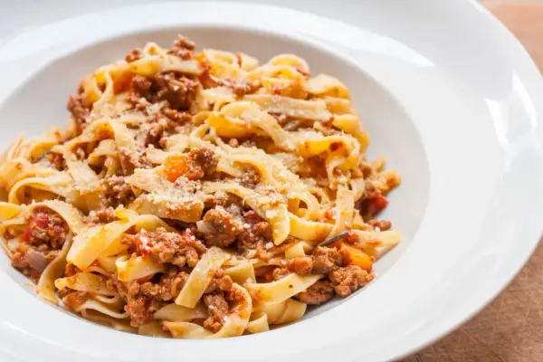 Pyszny makaron tagliatelle z bogatym sosem bolognese, posypany parmezanem. Idealny przepis na obiad.