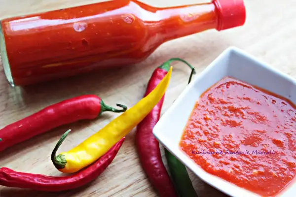 Pikantny sos z ostrej papryki w butelce i miseczce, obok świeże papryczki chili.