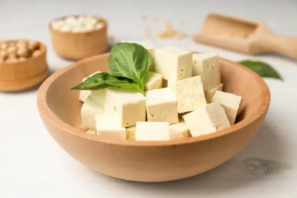 Kostki tofu w misce, ozdobione listkiem bazylii. Czy tofu można jeść na surowo? Tak, to świetna baza do sałatek.