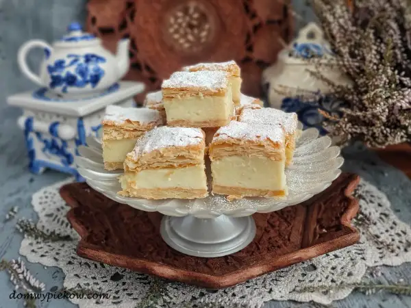 Kremowe napoleon ciasto, posypane cukrem pudrem, prezentuje się apetycznie na paterze.